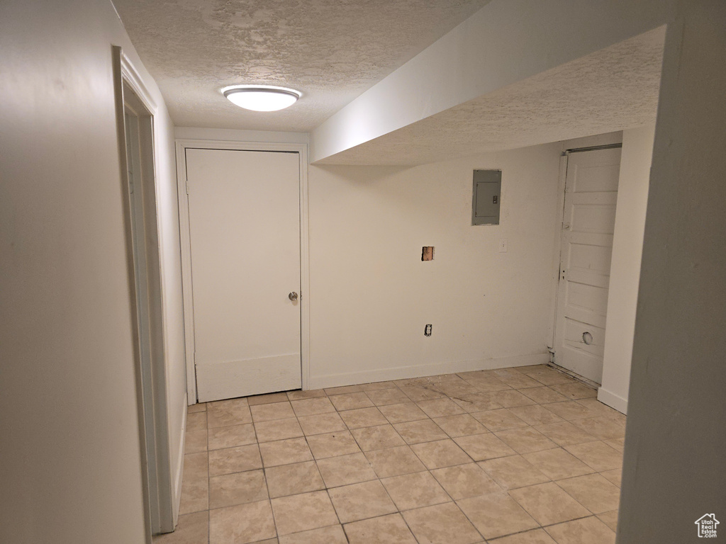 Finished below grade area with a textured ceiling, electric panel, and light tile patterned floors