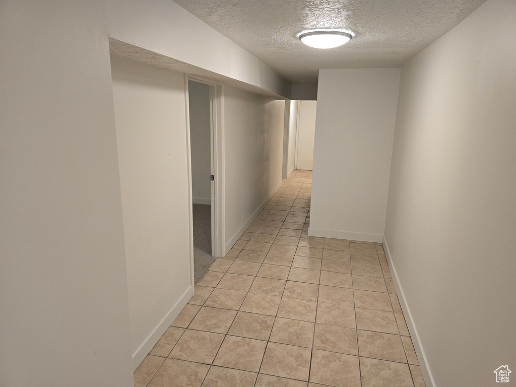 Corridor featuring a textured ceiling, light tile patterned flooring, and baseboards