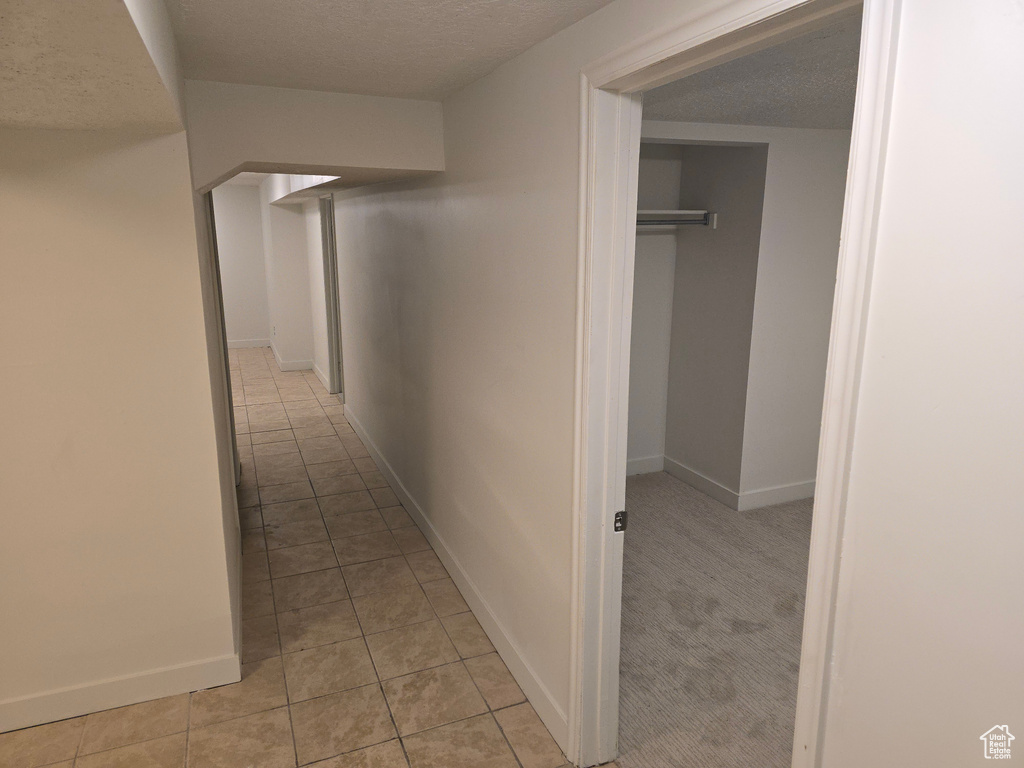 Corridor featuring light tile patterned floors, baseboards, and a textured ceiling