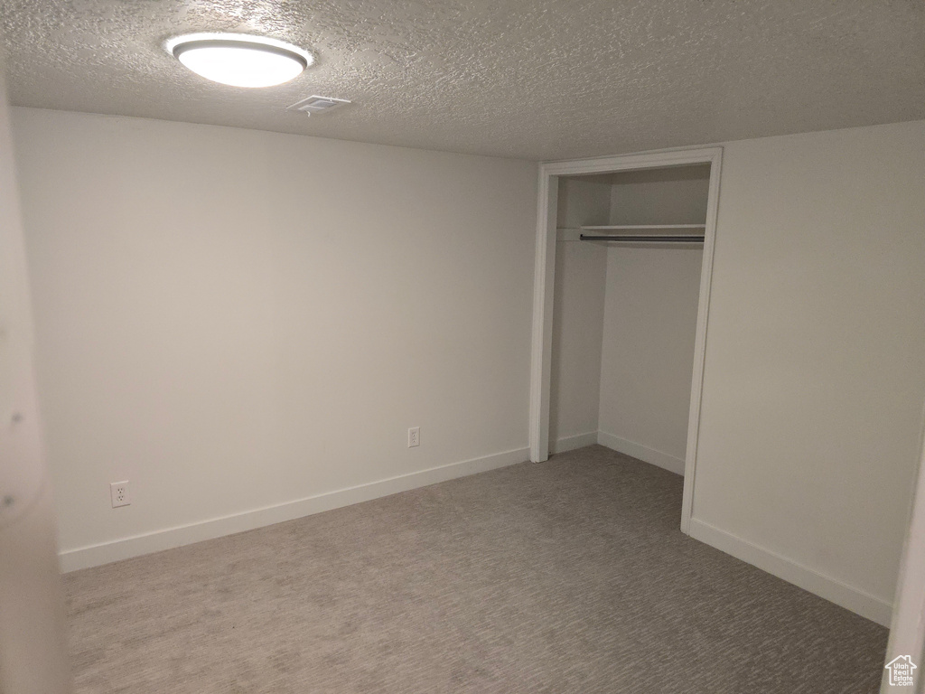 Unfurnished bedroom featuring a textured ceiling, carpet floors, a closet, and baseboards