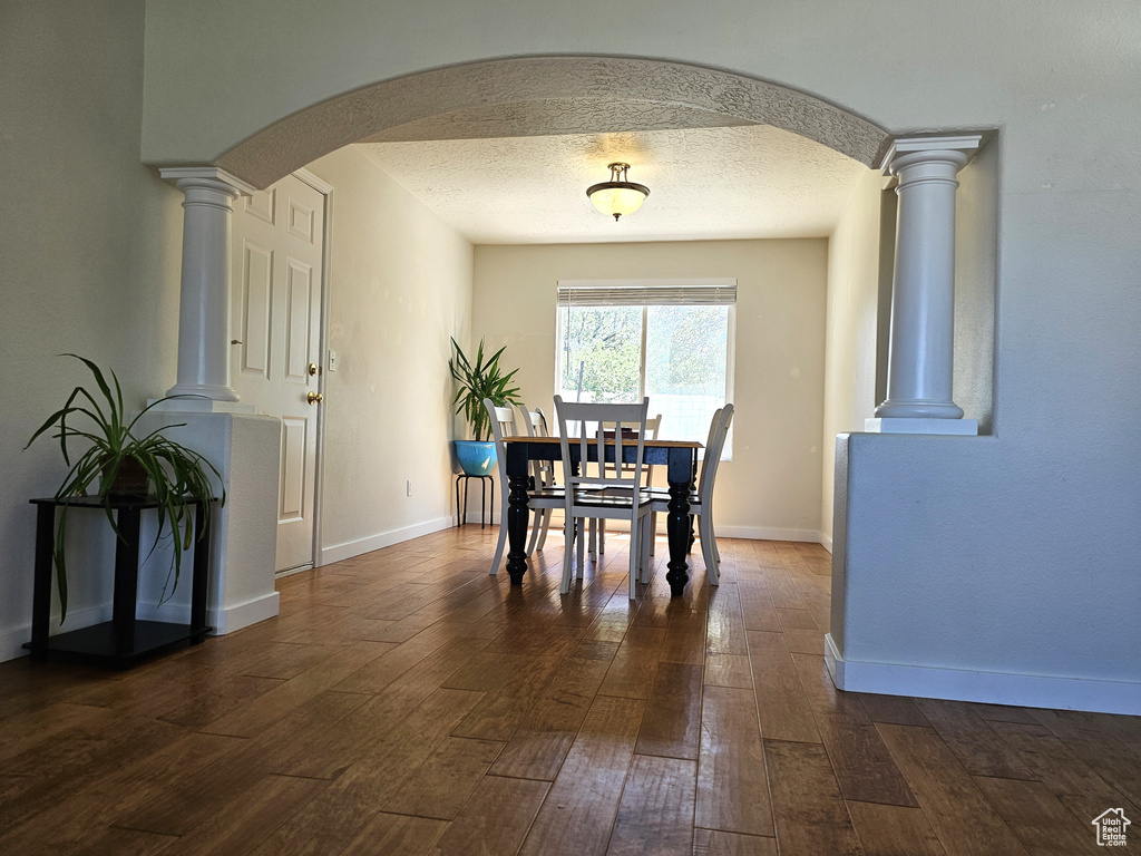 Dining area with arched walkways, dark wood finished floors, ornate columns, and baseboards