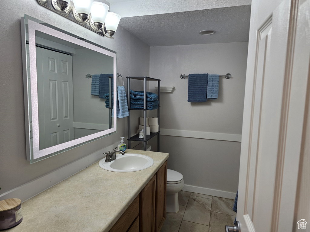 Bathroom with toilet, vanity, marble look tiles, and a textured ceiling