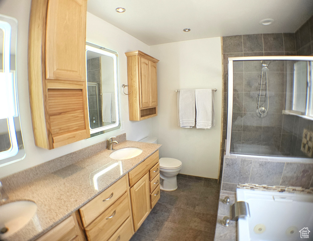Bathroom featuring a jetted tub, double vanity, tiled shower, and toilet