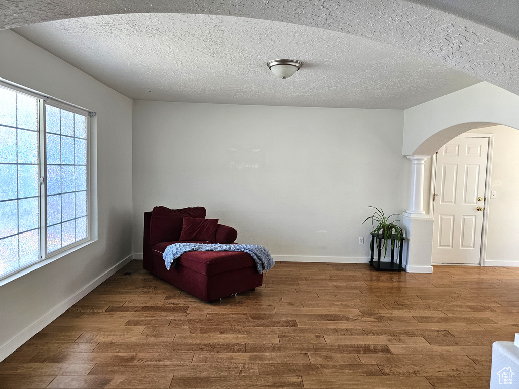 Sitting room with wood finished floors, arched walkways, baseboards, plenty of natural light, and a textured ceiling