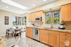 Kitchen featuring stainless steel dishwasher, a sink, white microwave, decorative backsplash, and light brown cabinets
