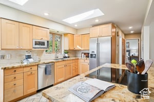 Kitchen featuring light brown cabinetry, stainless steel appliances, a skylight, light countertops, and a sink