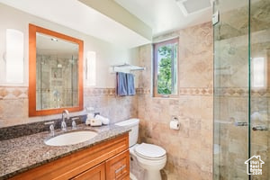 Bathroom with tile walls, vanity, a shower stall, and toilet