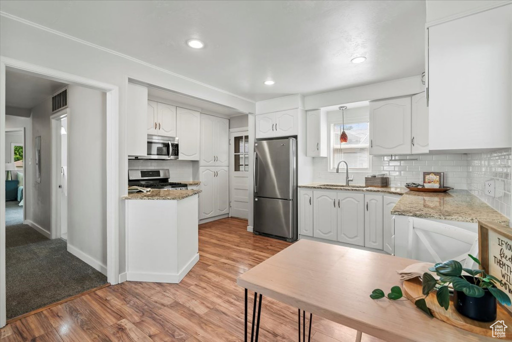 Kitchen with stainless steel appliances, a sink, backsplash, light wood-style floors, and white cabinets