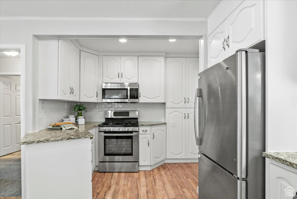 Kitchen featuring appliances with stainless steel finishes, white cabinetry, light wood finished floors, decorative backsplash, and crown molding