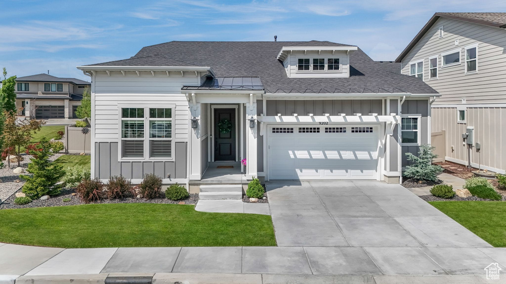View of front facade featuring board and batten siding, an attached garage, driveway, and a shingled roof