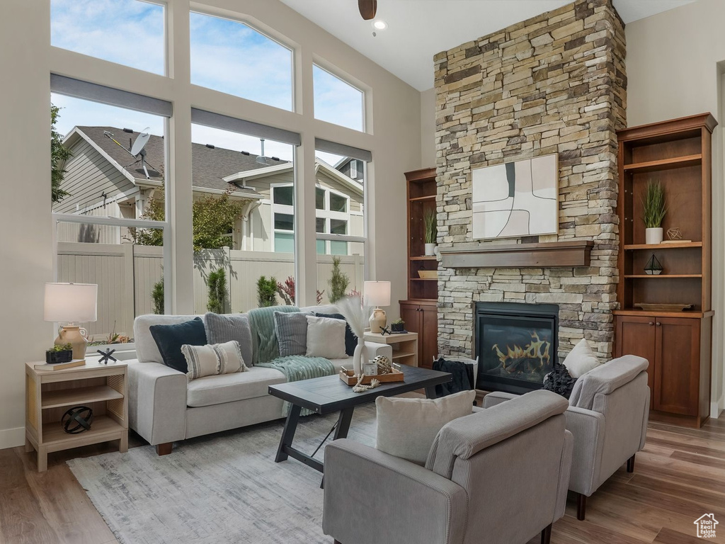 Living area with a stone fireplace, light wood-style flooring, baseboards, and a towering ceiling