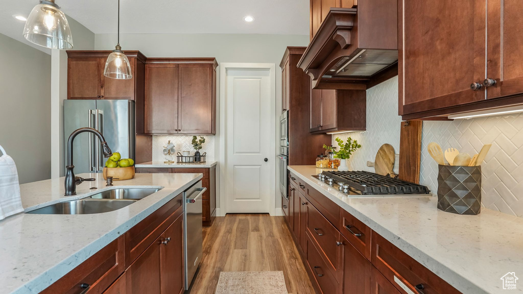 Kitchen featuring stainless steel appliances, a sink, custom exhaust hood, light wood-style flooring, and backsplash