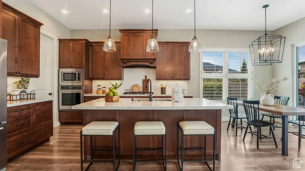 Kitchen with stainless steel appliances, light countertops, dark wood-type flooring, decorative backsplash, and a kitchen bar