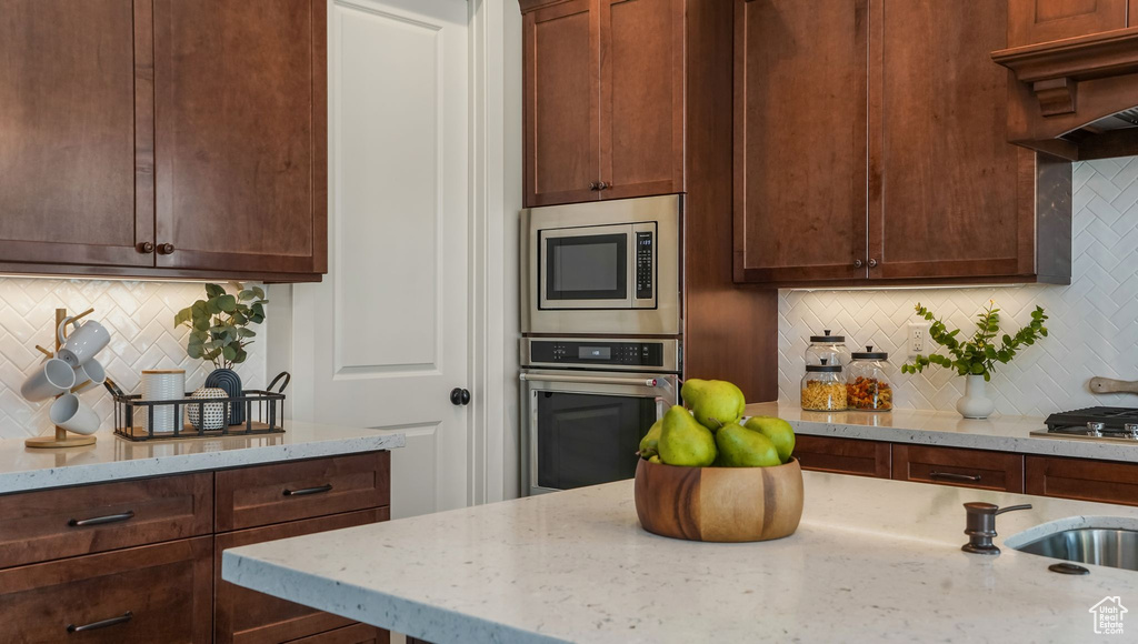 Kitchen with stainless steel appliances, backsplash, and light stone counters