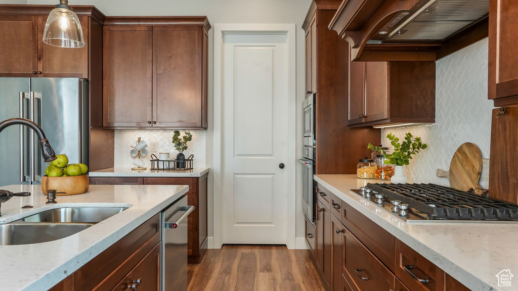 Kitchen with a sink, appliances with stainless steel finishes, dark wood-style flooring, premium range hood, and decorative backsplash