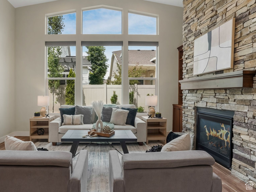 Living area featuring a stone fireplace, baseboards, wood finished floors, and a high ceiling