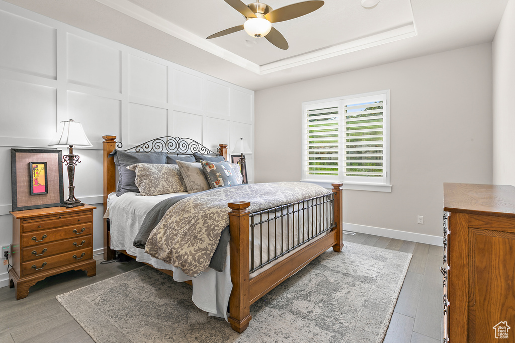 Bedroom featuring wood finished floors, a raised ceiling, and ceiling fan