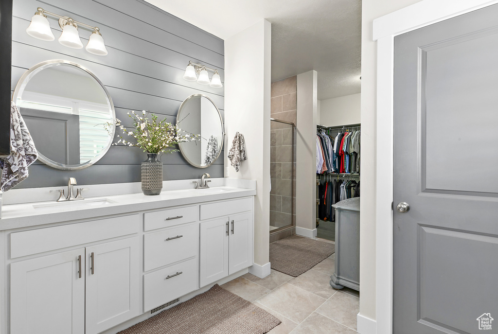 Full bathroom featuring double vanity, a tile shower, tile patterned flooring, a spacious closet, and baseboards