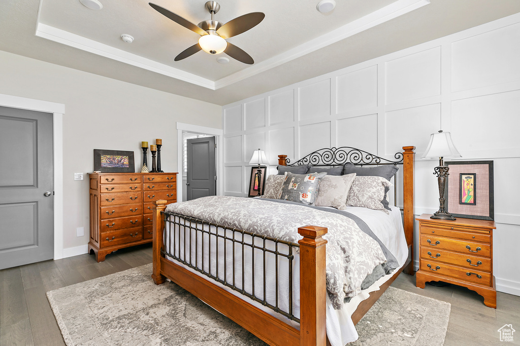 Bedroom with a raised ceiling, a decorative wall, wood finished floors, ornamental molding, and ceiling fan