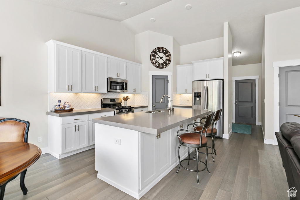 Kitchen with appliances with stainless steel finishes, a sink, decorative backsplash, light wood-style flooring, and high vaulted ceiling