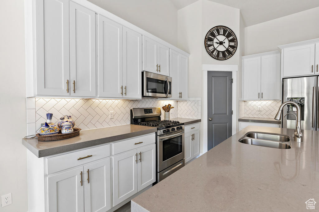 Kitchen with stainless steel appliances, a sink, backsplash, white cabinets, and light stone counters