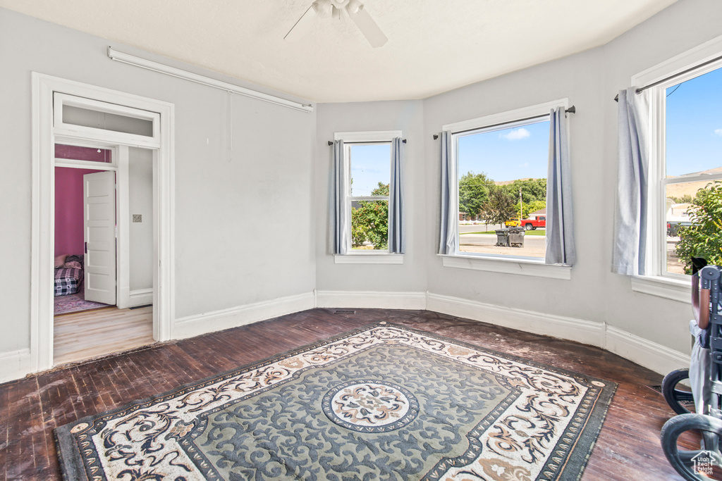 Unfurnished room with ceiling fan, wood finished floors, plenty of natural light, and baseboards