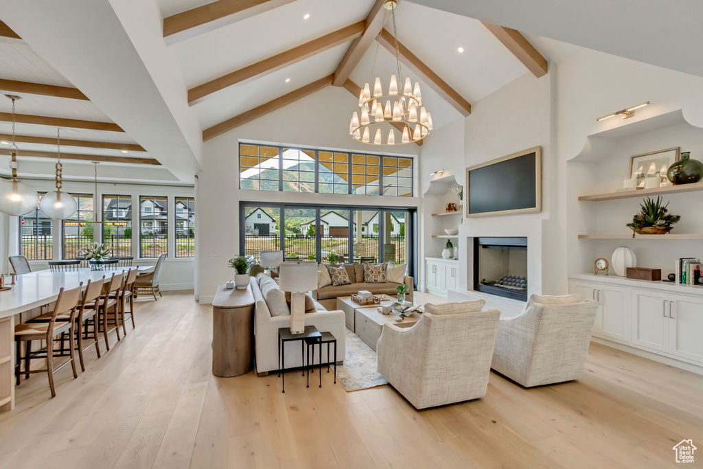 Living room featuring beam ceiling, light wood finished floors, a chandelier, a fireplace, and healthy amount of natural light