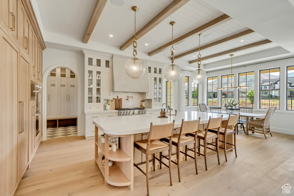 Kitchen with light wood finished floors, a large island with sink, a kitchen breakfast bar, open shelves, and beamed ceiling