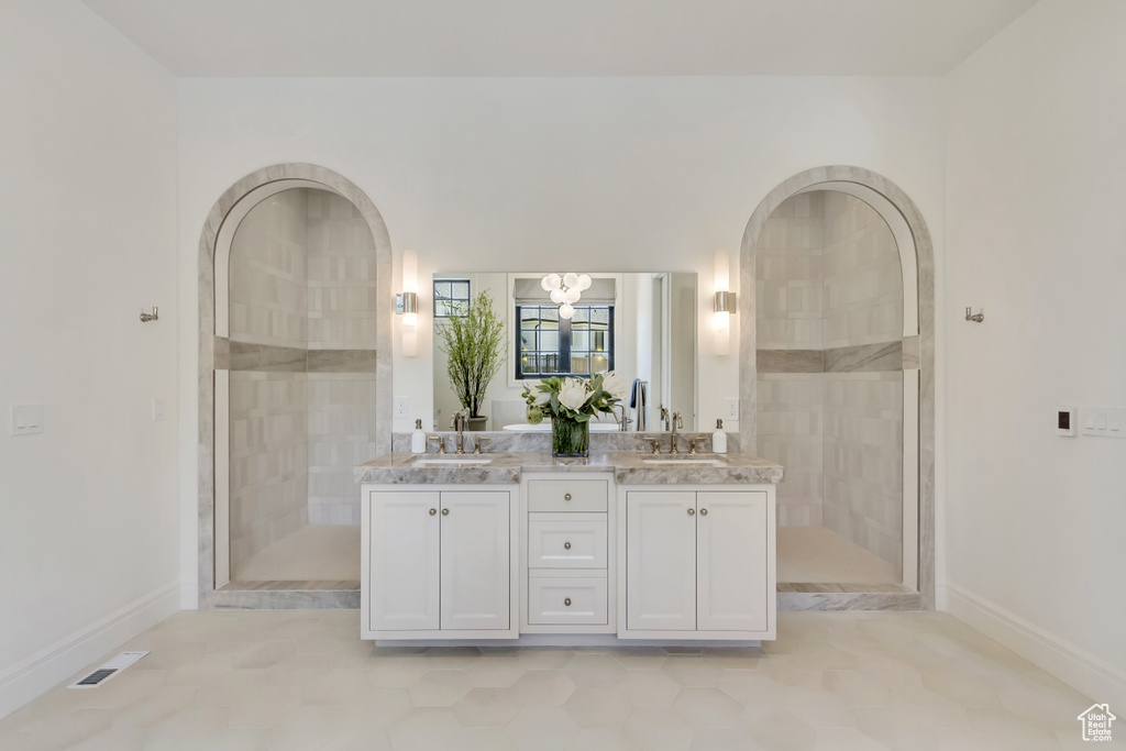 Full bath featuring double vanity, tiled shower, a chandelier, and tile patterned floors