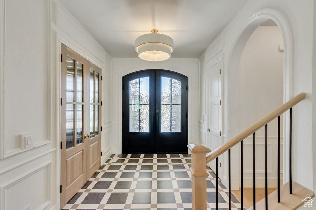 Foyer entrance featuring a decorative wall, french doors, arched walkways, and stairway
