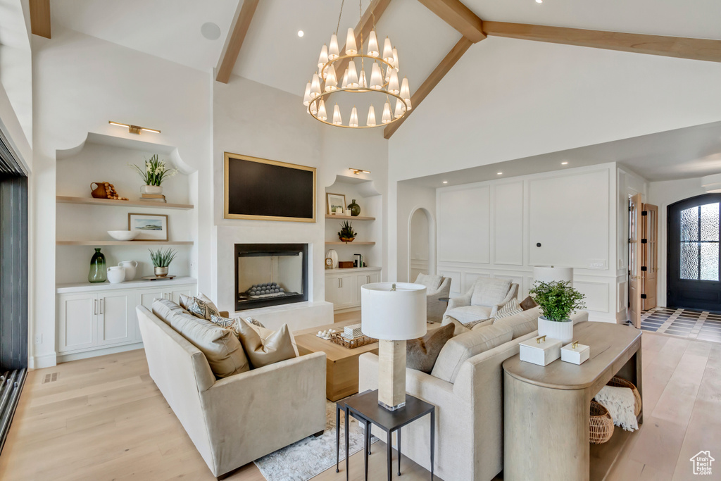 Living room with built in features, high vaulted ceiling, light wood-style floors, beamed ceiling, and a chandelier