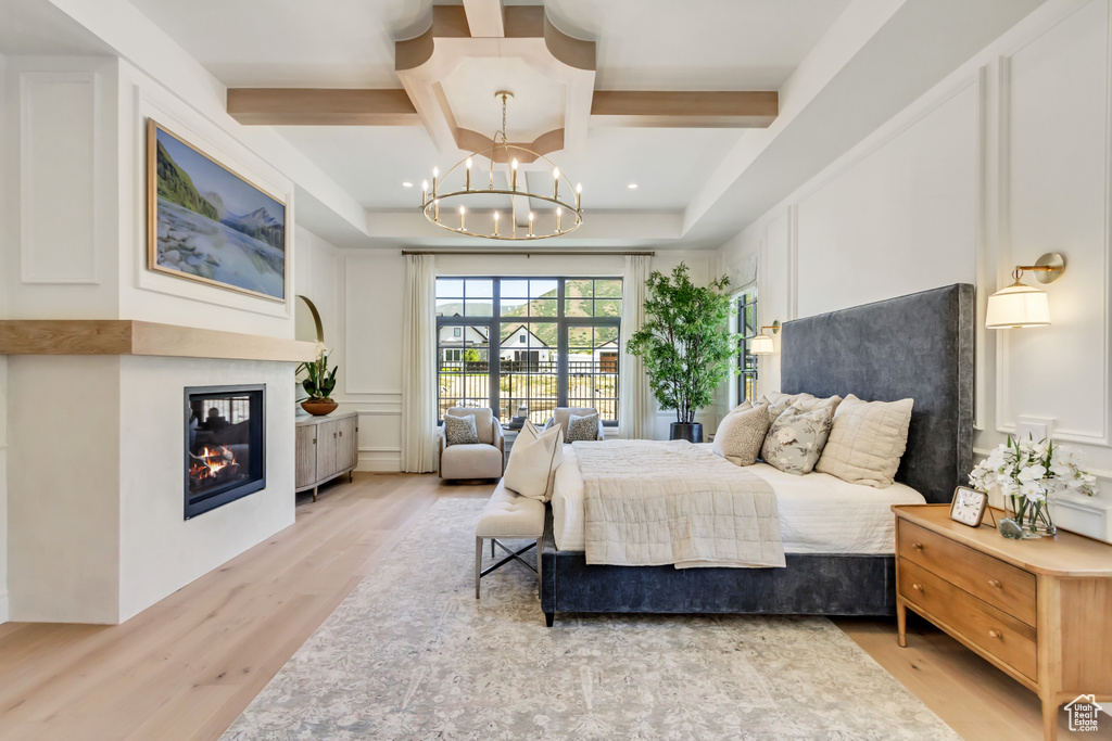 Bedroom featuring coffered ceiling, light wood-type flooring, a glass covered fireplace, a chandelier, and a decorative wall