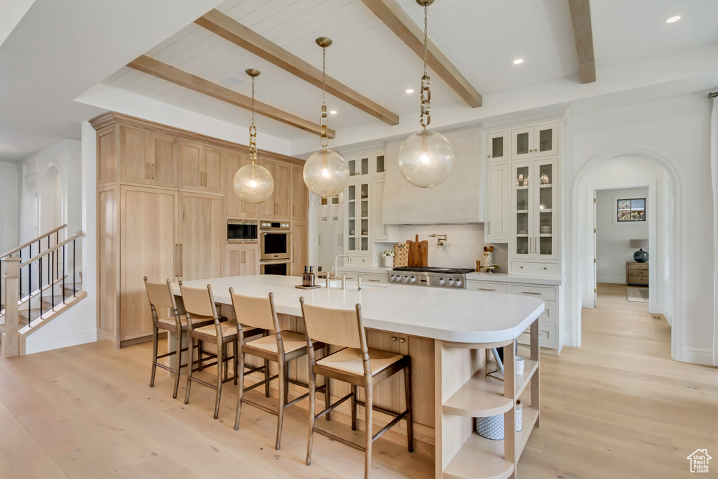 Kitchen featuring arched walkways, open shelves, double oven, light wood-type flooring, and a kitchen bar