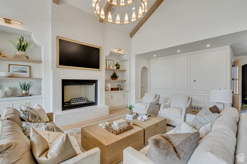 Living room with built in features, a fireplace with raised hearth, high vaulted ceiling, a chandelier, and light wood-style floors