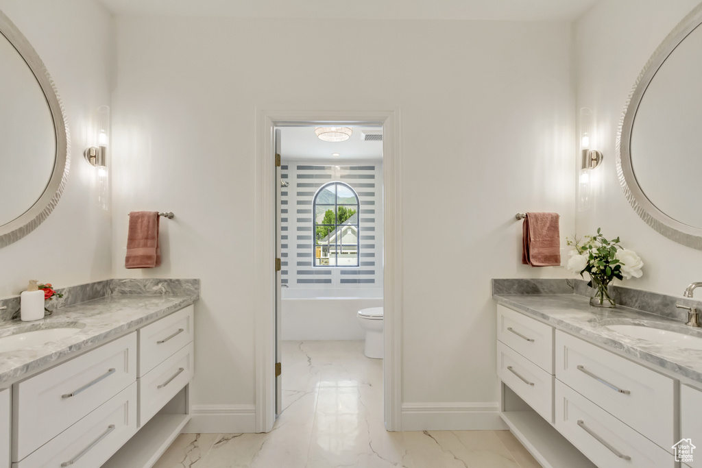 Full bathroom with marble finish flooring, two vanities, and a bath