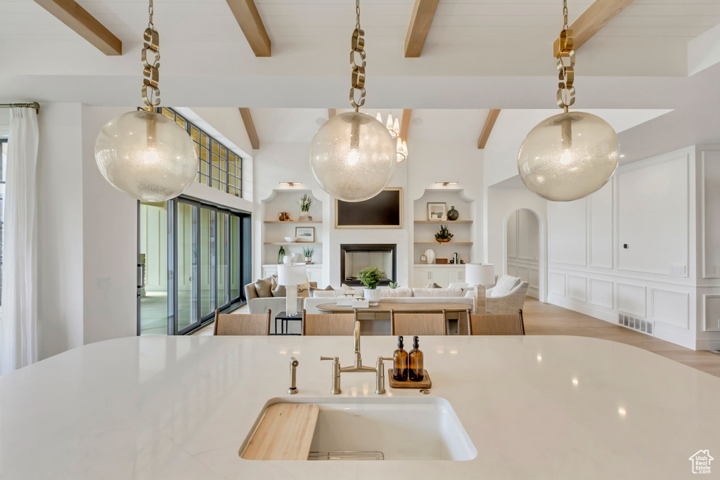 Kitchen featuring a sink, beam ceiling, open floor plan, light countertops, and hanging light fixtures