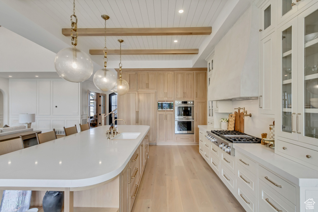 Kitchen with a sink, light wood-style flooring, appliances with stainless steel finishes, light countertops, and wooden ceiling with exposed beams