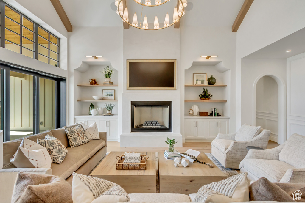 Living room featuring built in shelves, beamed ceiling, a fireplace with raised hearth, a towering ceiling, and a chandelier