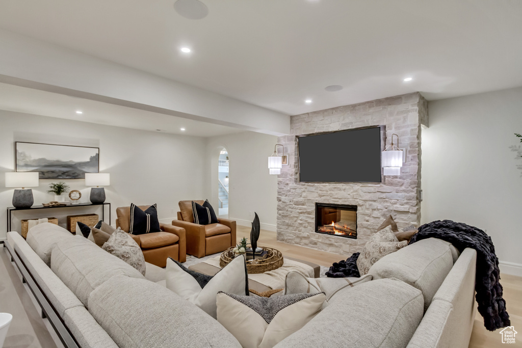 Living area with a stone fireplace, recessed lighting, light wood-style flooring, beam ceiling, and arched walkways