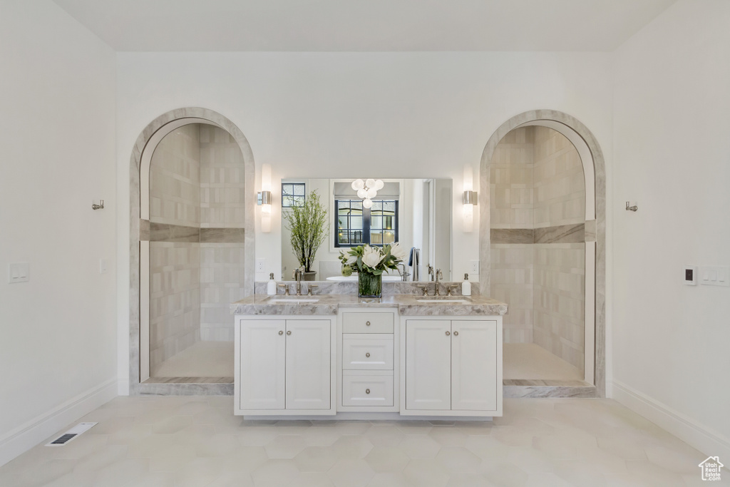Bathroom featuring double vanity, a tile shower, and a chandelier