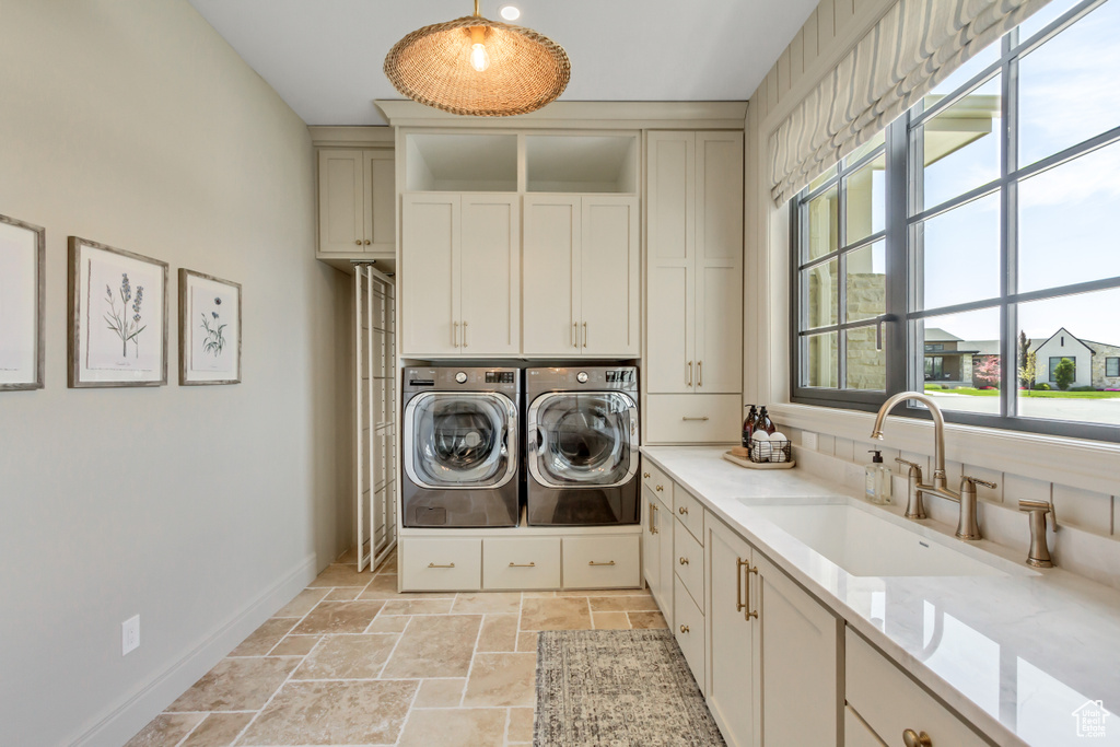 Washroom with washer and clothes dryer, cabinet space, healthy amount of natural light, and stone tile floors