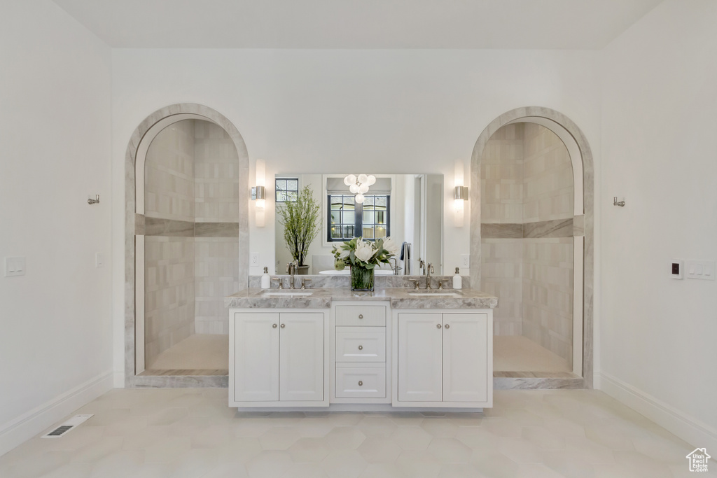 Bathroom featuring double vanity, a tile shower, and a chandelier