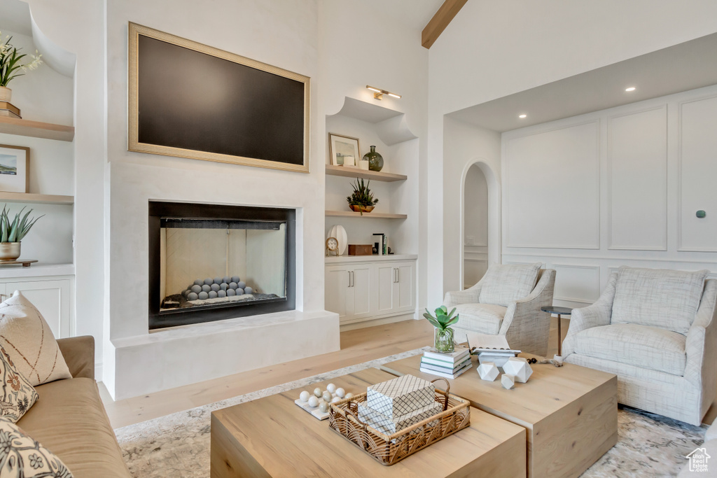 Living room with built in shelves, a fireplace with raised hearth, light wood-style floors, high vaulted ceiling, and beam ceiling