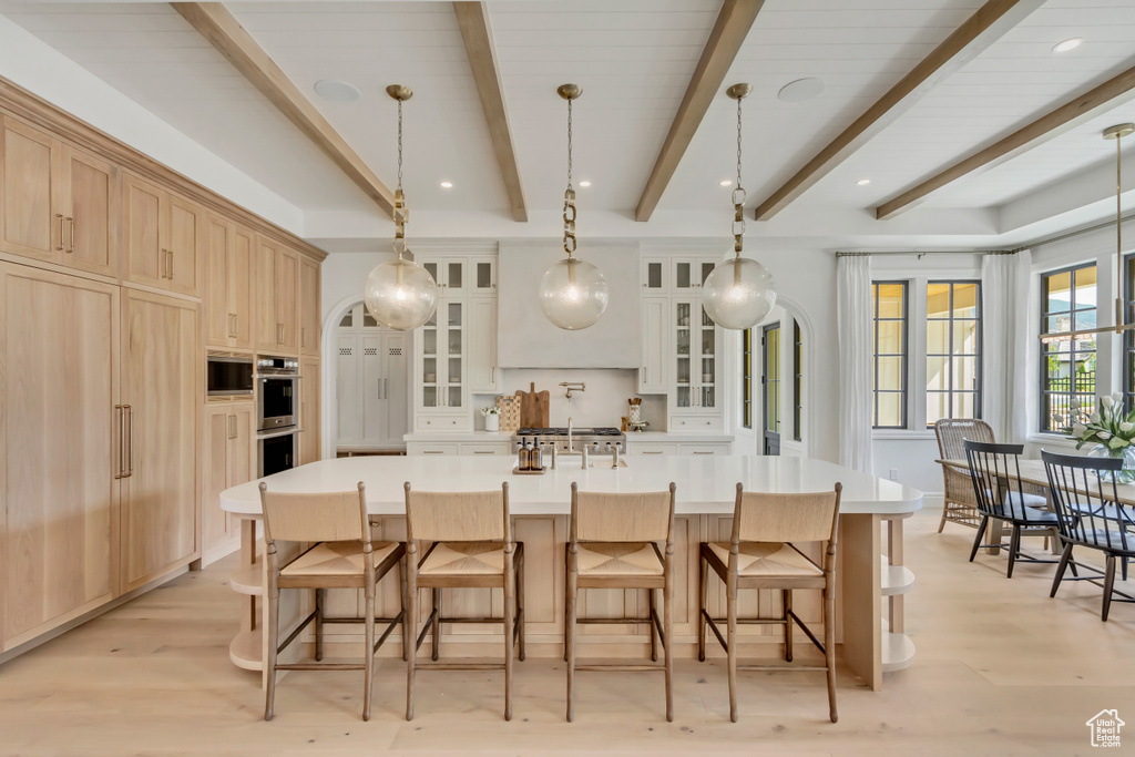 Kitchen featuring beamed ceiling, light brown cabinets, glass insert cabinets, light countertops, and a spacious island