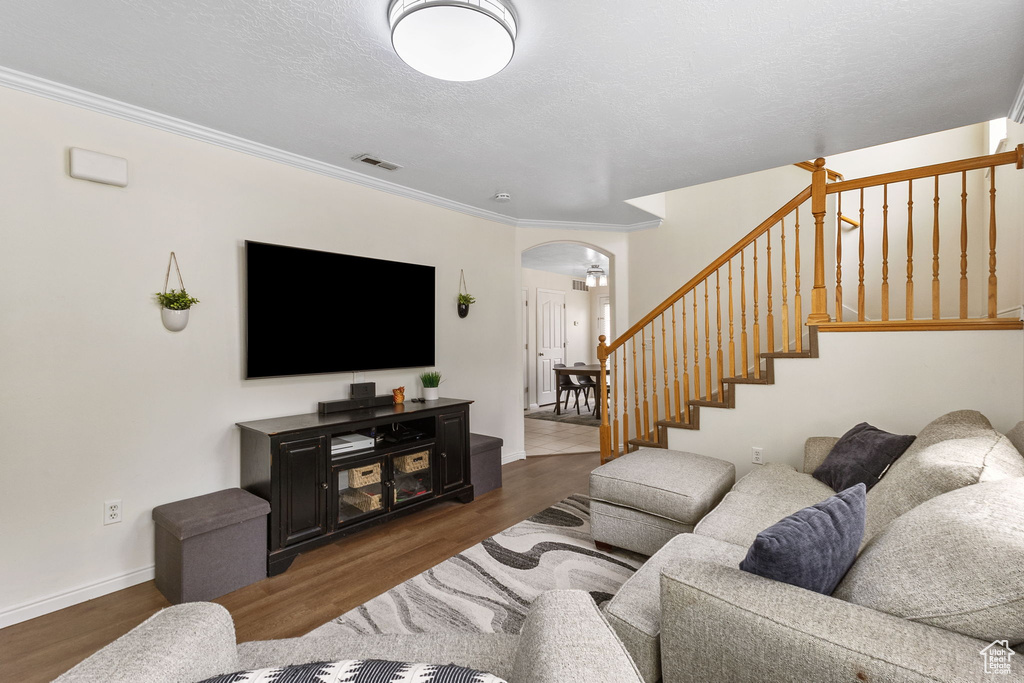 Living room featuring arched walkways, stairway, wood finished floors, baseboards, and crown molding