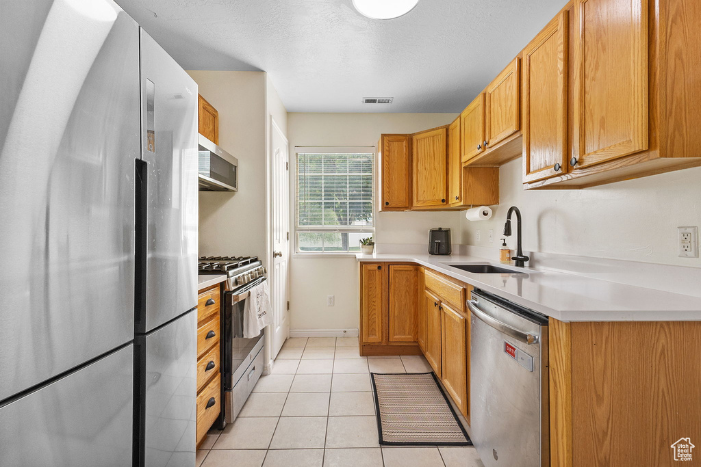 Kitchen featuring stainless steel appliances, a sink, light countertops, light tile patterned floors, and baseboards