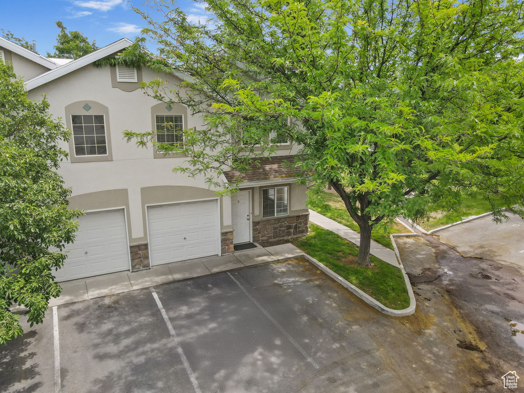 View of front facade featuring stone siding, stucco siding, driveway, and an attached garage