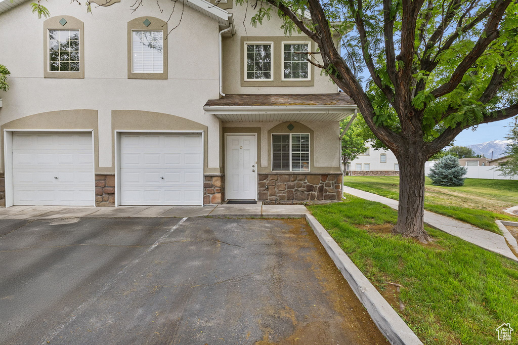 Townhome / multi-family property with stone siding, an attached garage, asphalt driveway, and stucco siding