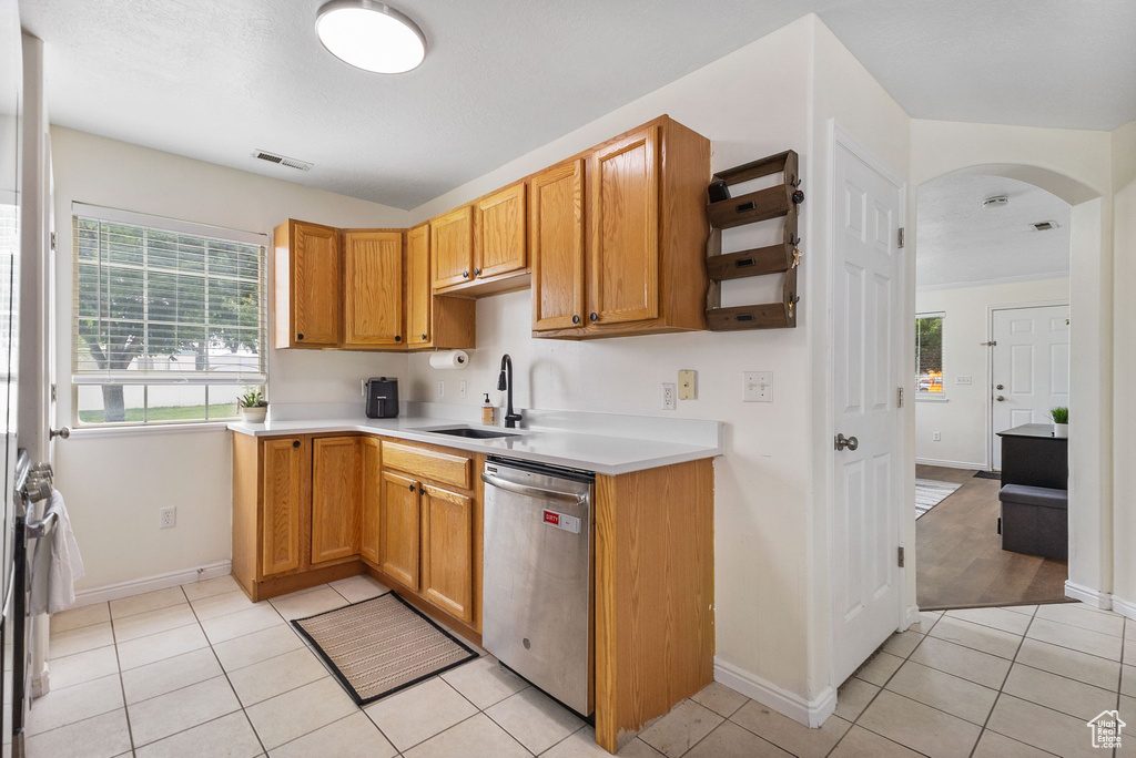 Kitchen featuring dishwasher, light tile patterned flooring, arched walkways, light countertops, and baseboards