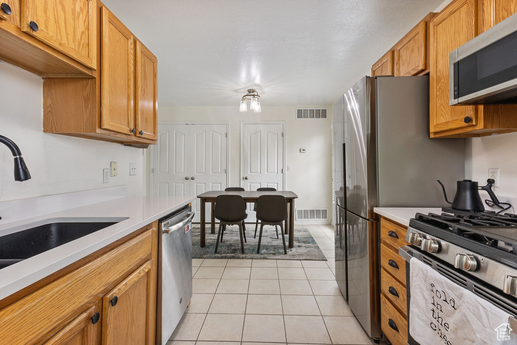 Kitchen with stainless steel appliances, a sink, light countertops, and light tile patterned floors